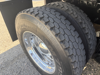 Truck dual rear axle tire close-up showing heavy-duty tread and chrome wheel; part of Mack GR64F dump truck undercarriage.