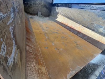 Dump bed interior of a 2025 Mack GR64F showing scratched metal bed with rust-colored wear and side panels.