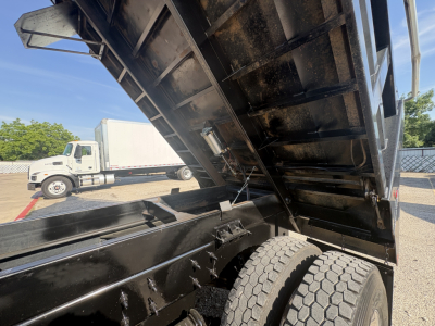 Dump truck bed raised showing hydraulic mechanism and dual rear wheels on a Mack GR64F chassis.