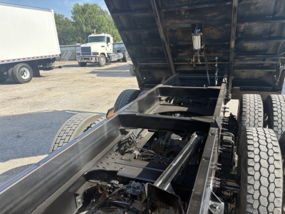 Mack GR64F dump truck chassis with raised bed showing frame, hydraulic cylinders, and rear axles.