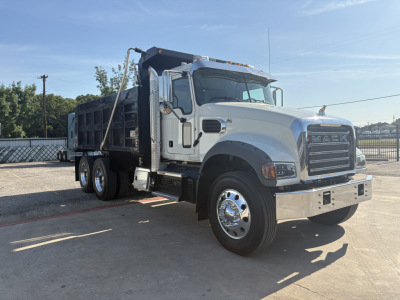 Truck cab and dump bed of a Mack GR64F dump truck, side view, white cab with chrome bumper and dual rear axles.