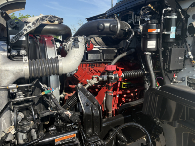 Mack GR64F engine bay showing red engine block, air intake, hoses, and various components in a truck engine compartment.