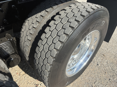 Front dual rear tire of a Mack GR64F dump truck showing dual tread, polished chrome wheel, and part of hydraulic components.
