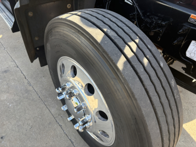 Truck front wheel of a 2025 Mack GR64F dump truck showing a single front dual rear? Actually image shows front dual? It shows a single front axle wheel with large drum? Type: wheel and tire with lug nuts and chrome hub.