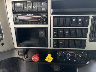 Mack GR64F interior driver-side dash showing gear selector (R N D L), engine start switch, radio, control switches, red and yellow trailer air switches, and climate controls.