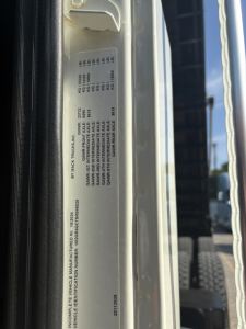 Tag with vehicle specification text on Mack GR64F side, listing model, weights, and manufacturing details.