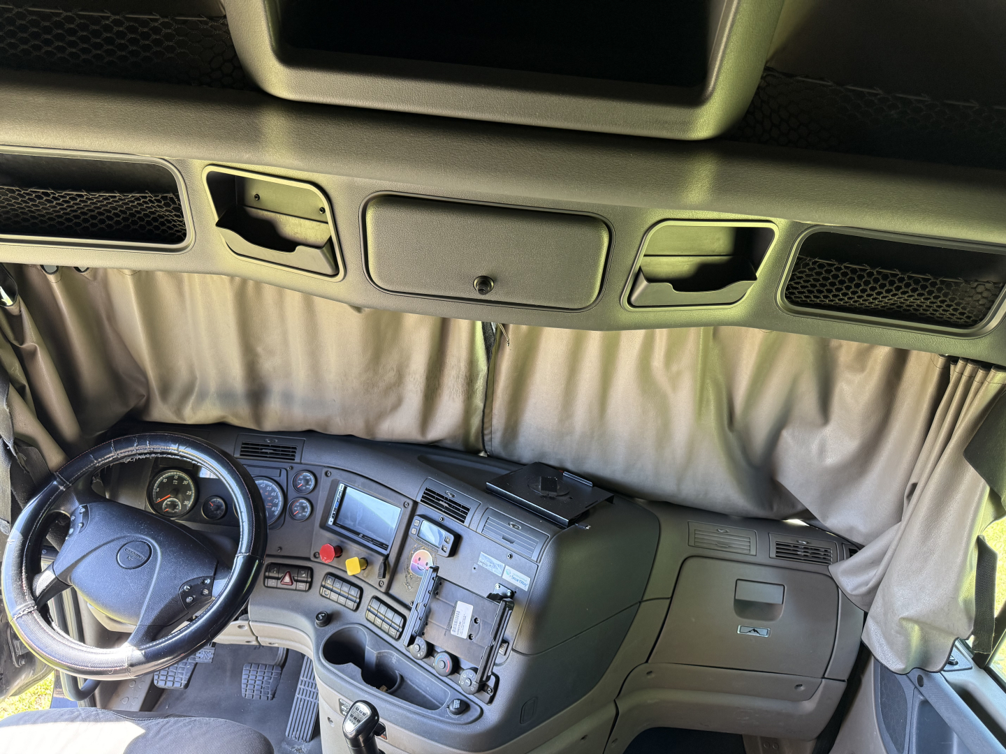 Truck cab interior of a 2016 Freightliner Cascadia Evolution showing dashboard with steering wheel, gauges, center console, and curtain behind.