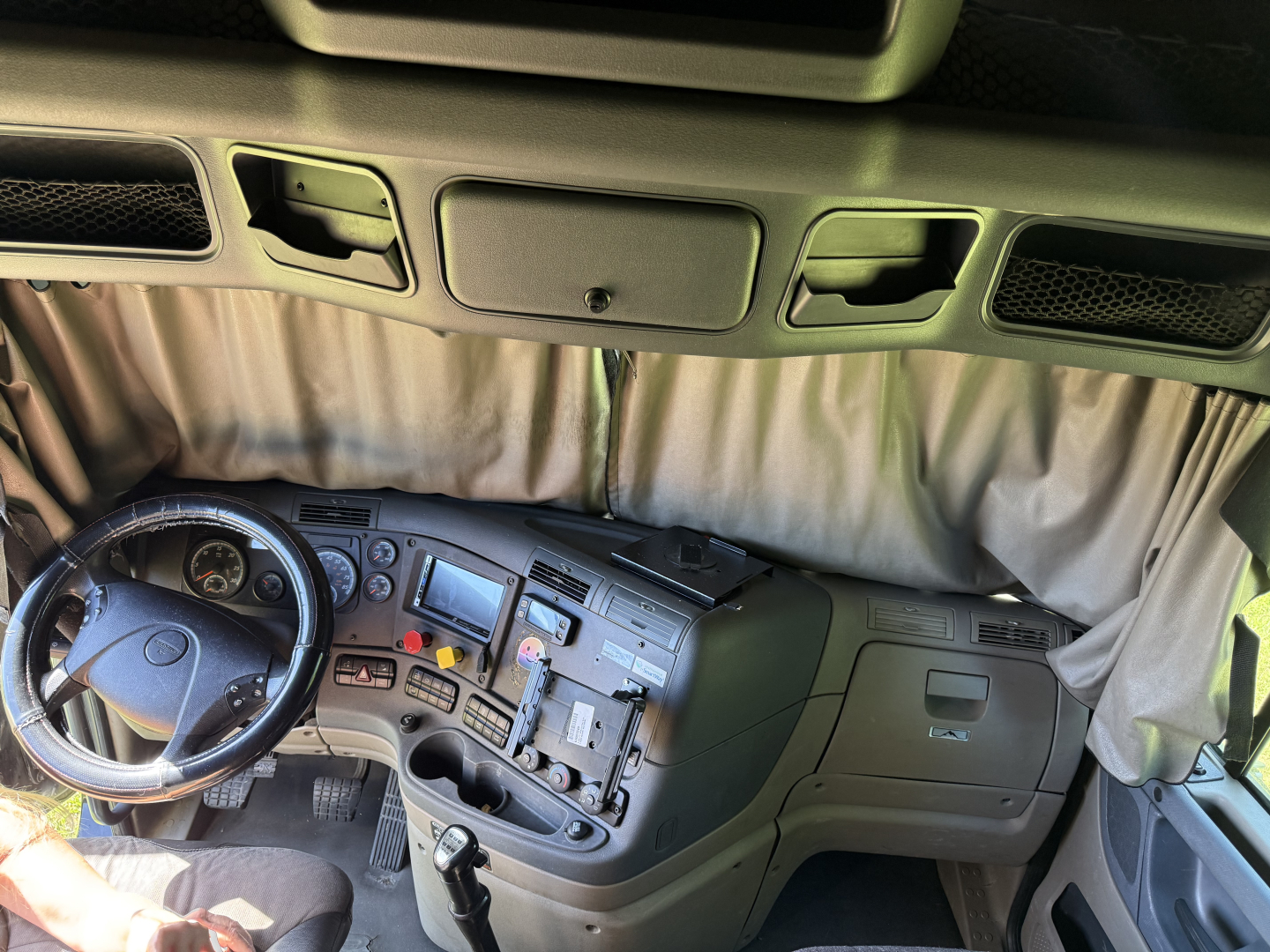 Cab interior of a 2016 Freightliner Cascadia Evolution in view from the passenger side, showing steering wheel, dashboard with gauges and controls, center console, and sleeper area curtain.