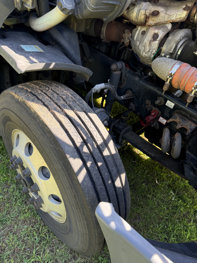 Front left wheel and engine bay of a Freightliner Cascadia Evolution truck showing tire tread and exposed engine parts.
