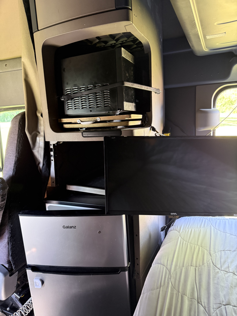 Cab interior of a 2016 Freightliner Cascadia Evolution showing a shelf with a microwave, a small fridge, and a flat screen monitor.