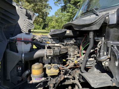 Truck engine bay of a 2016 Freightliner Cascadia Evolution showing multiple fluid reservoirs, hoses, and wiring harnesses.