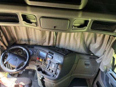 Cab interior of a 2016 Freightliner Cascadia Evolution in view from the passenger side, showing steering wheel, dashboard with gauges and controls, center console, and sleeper area curtain.