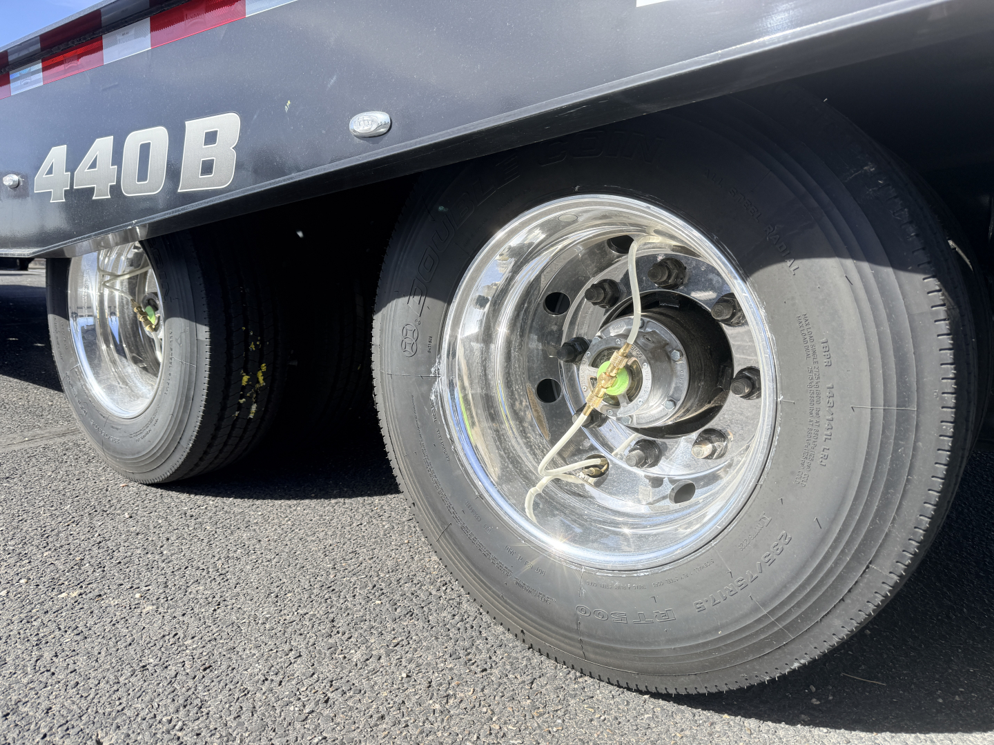 Landoll trailer wheel area showing dual axles and polished rims; number 440B on trailer side; lug nuts and hub with center nut visible.