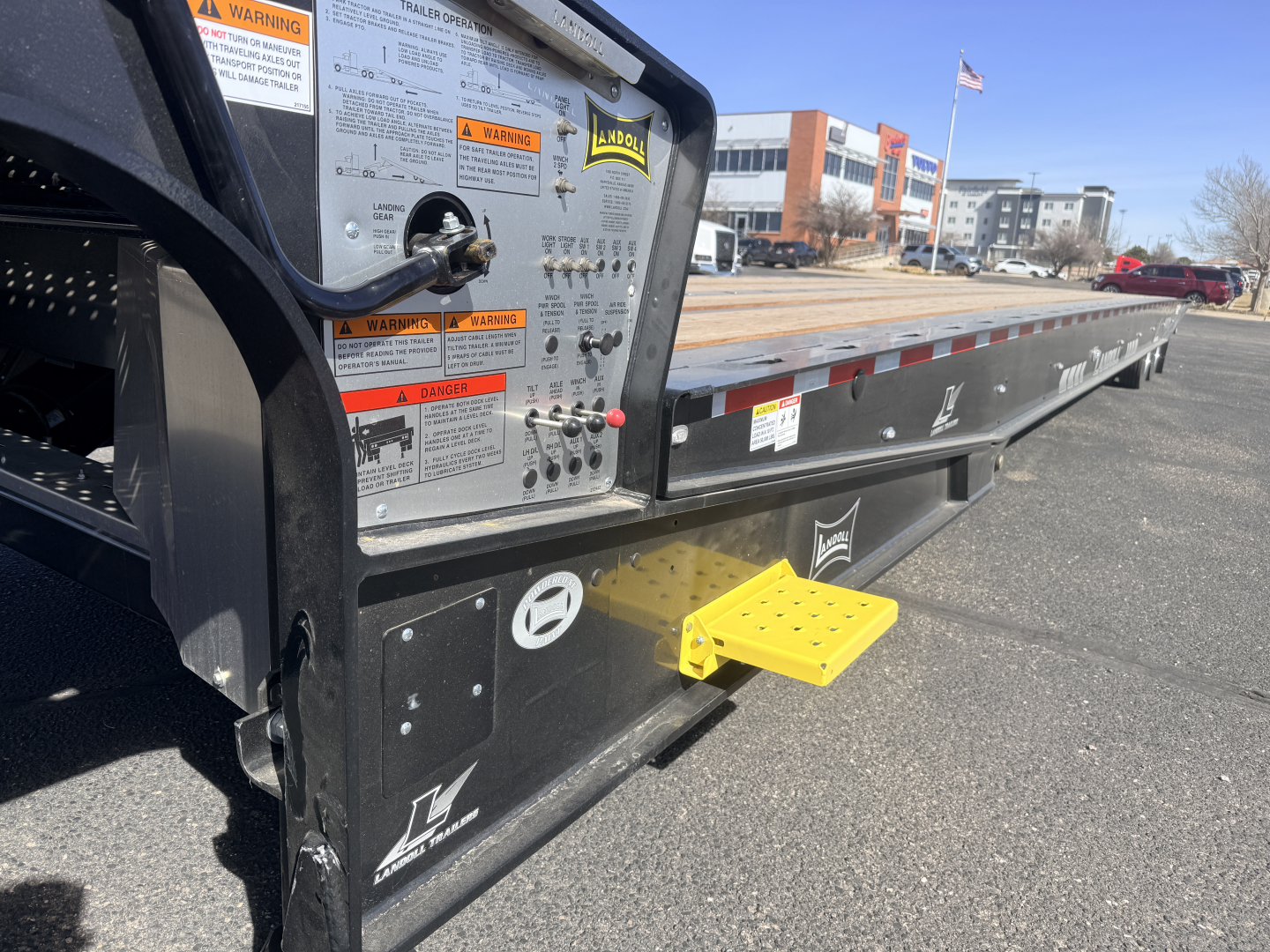 Trailer deck side of a 2027 Landoll 440B-53 40-ton traveling axle lowboy trailer showing side panels, warning labels, and yellow entry step.