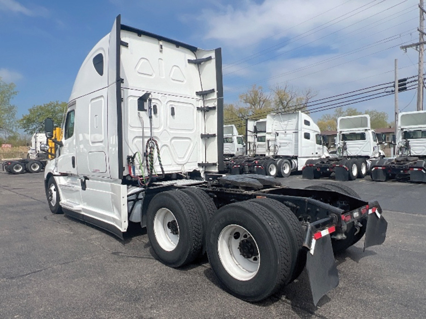 Truck chassis in a lot showing a 2022 Freightliner Cascadia126 rear view with dual rear axles, exposed fifth wheel area, and sleeper cab in a light gray color.