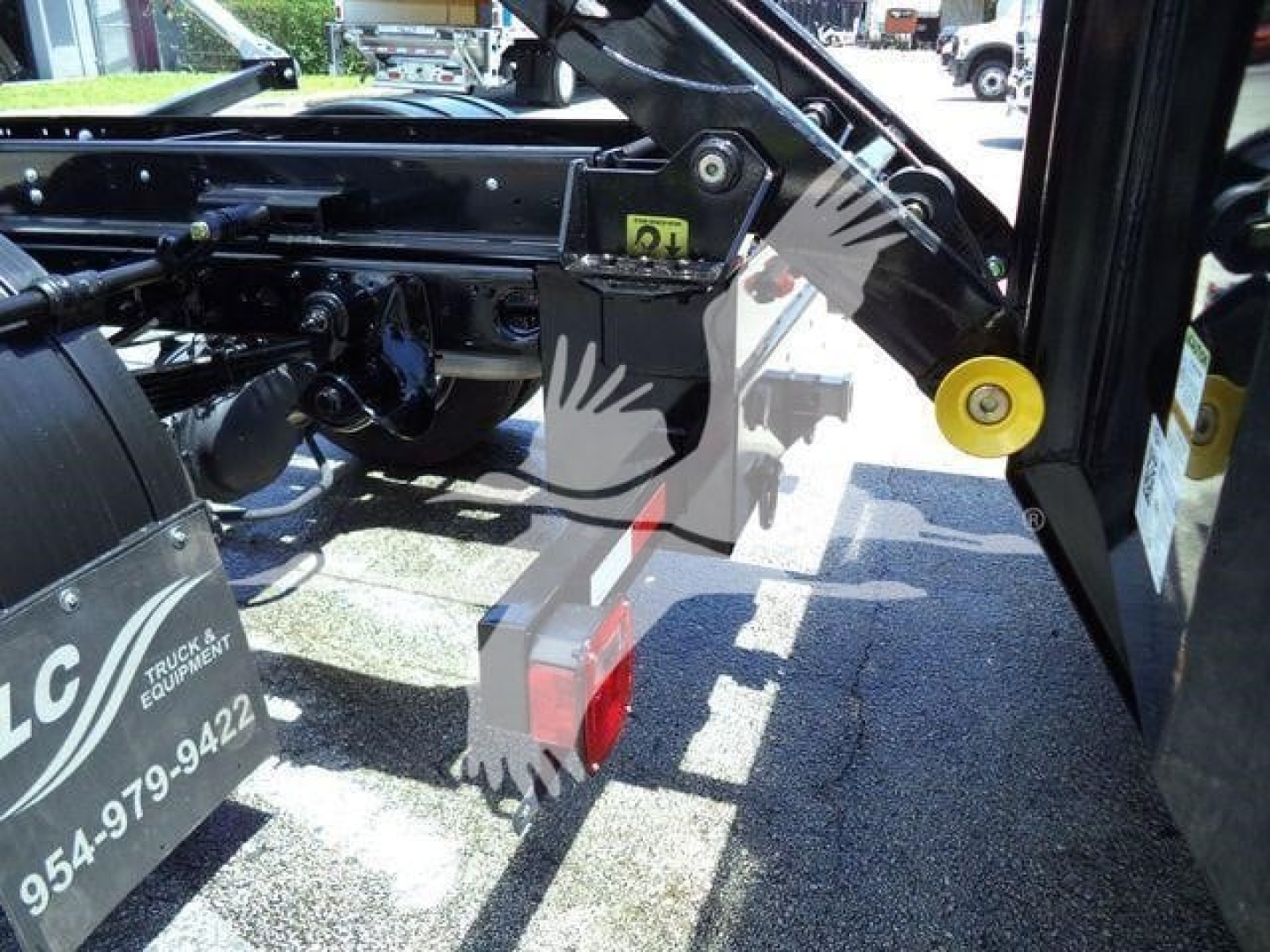Ram truck hooklift mounting hardware with hydraulic bracket and yellow hinge, side view showing black chassis and red hitch block.