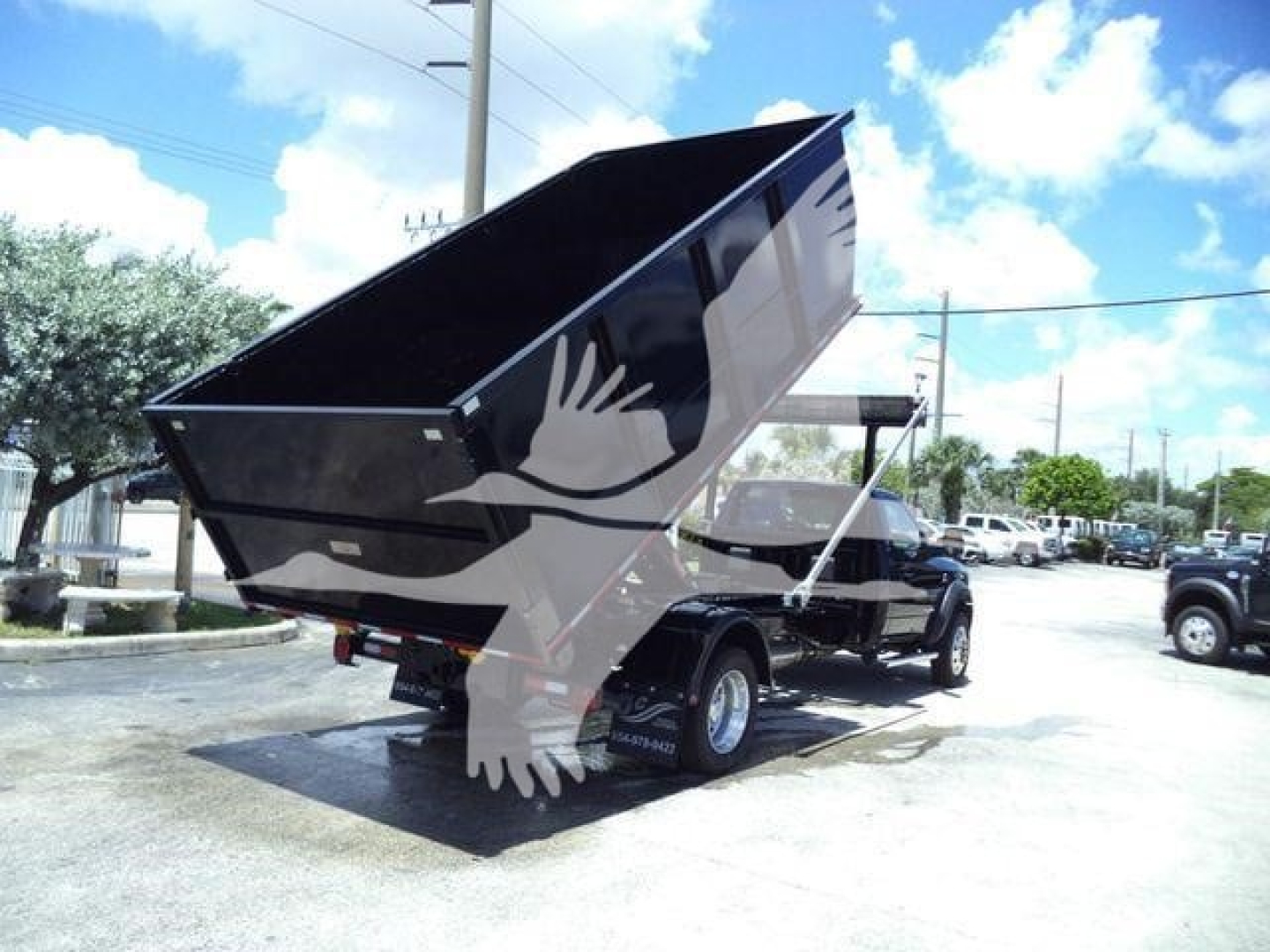 Ram 5500 SLT dump bed truck with hooklift frame and black dumping bed, rear view showing lifted bed in a dealership lot.