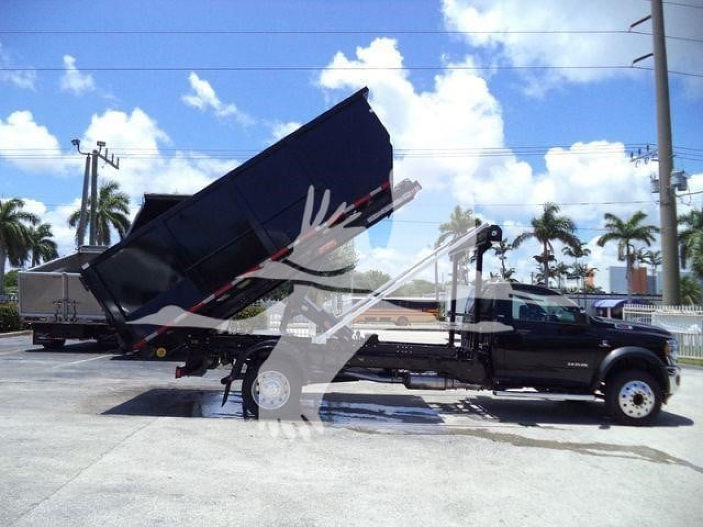Ram 5500 SLT dump truck in service with a raised dump bed on a hooklift chassis; black truck with long wheelbase and dual rear wheels visible.