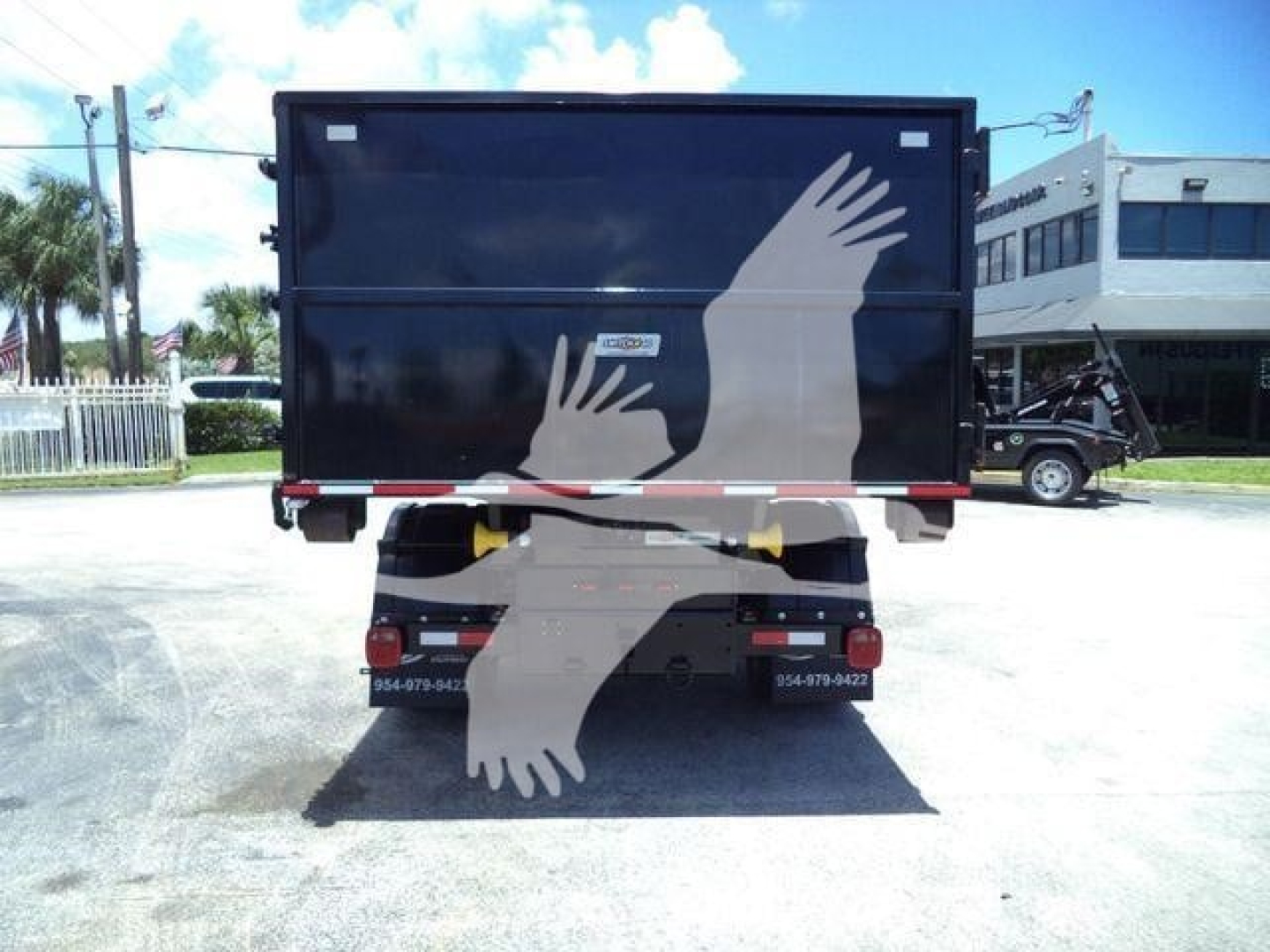 Truck bed seen from rear showing hooklift body with Ram 5500 SLT; license plate area blurred and dealership stickers visible.