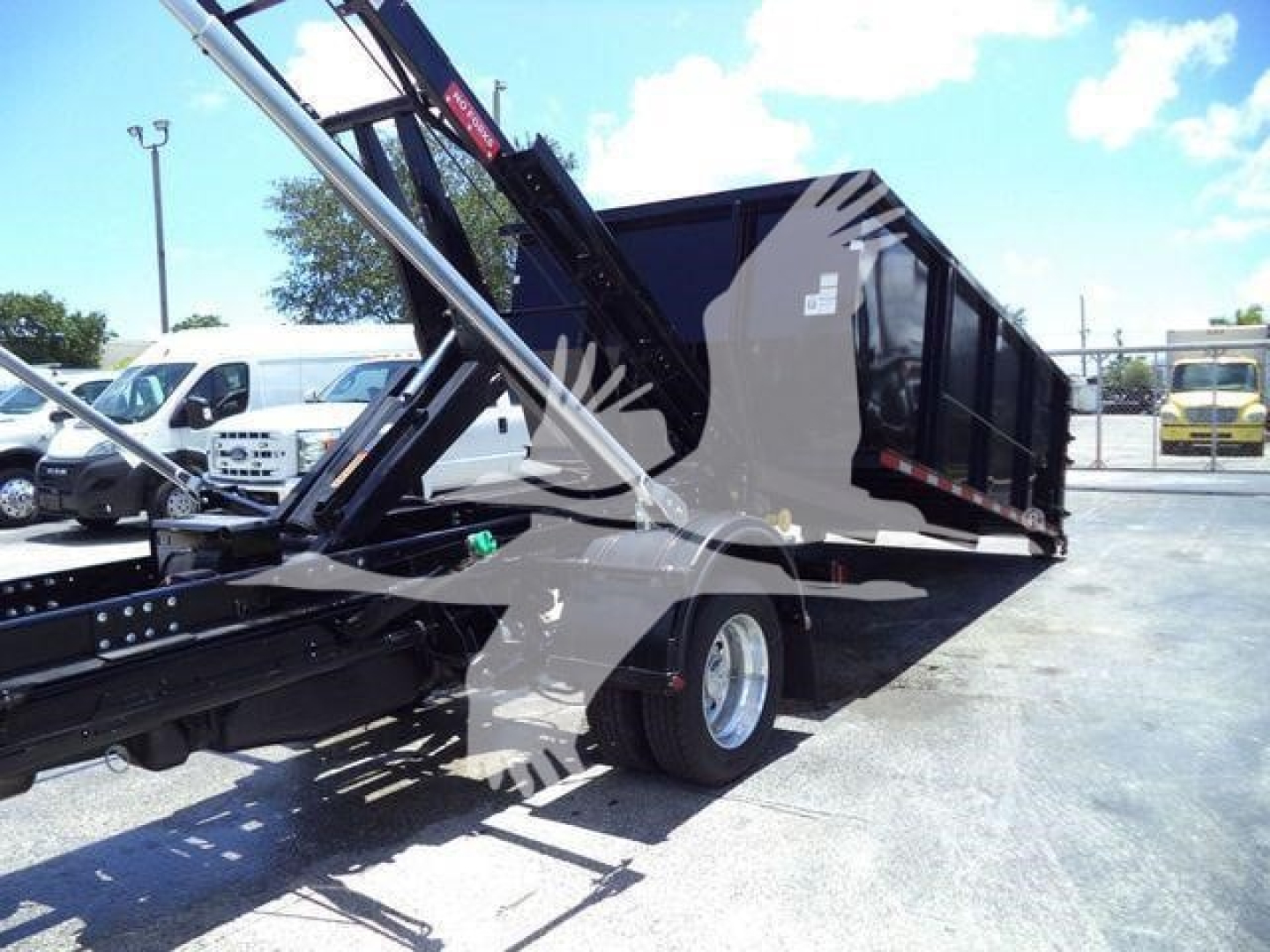 Ram 5500 SLT hooklift truck with black dump bed and hydraulic arms, side view showing extended lift mechanism.