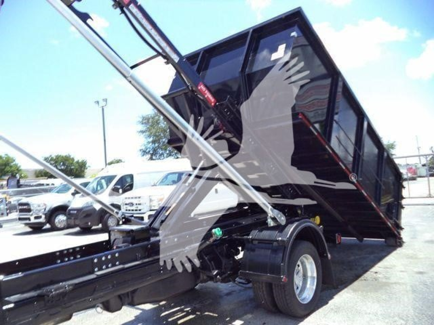 Ram 5500 SLT dump bed/ hooklift truck with hydraulic arm raised, side view showing front wheel and hydraulic cylinder.
