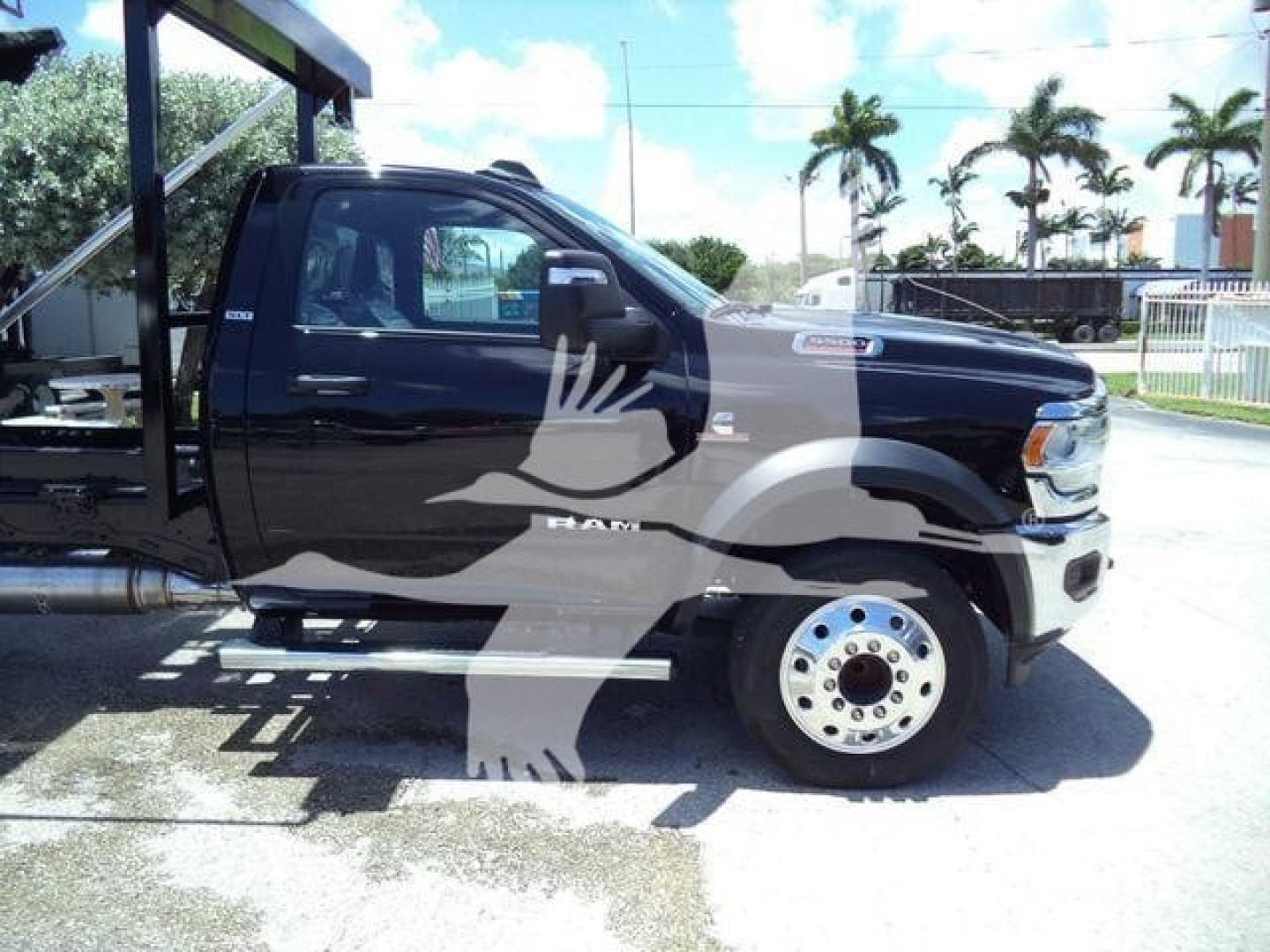 Truck side view showing a black 2024 Ram 5500 SLT hooklift with side steps and large front tire, visible badges on door and hood, dealership lot in background.
