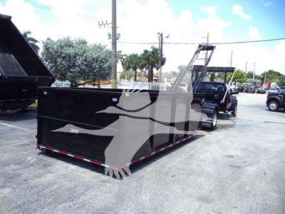 Ram 5500 SLT hooklift truck with a long black dump/deck body in a parking lot; stock number DSL550014SNG1FM; category hooklift; new vehicle; backdrop shows other trucks and palm trees.
