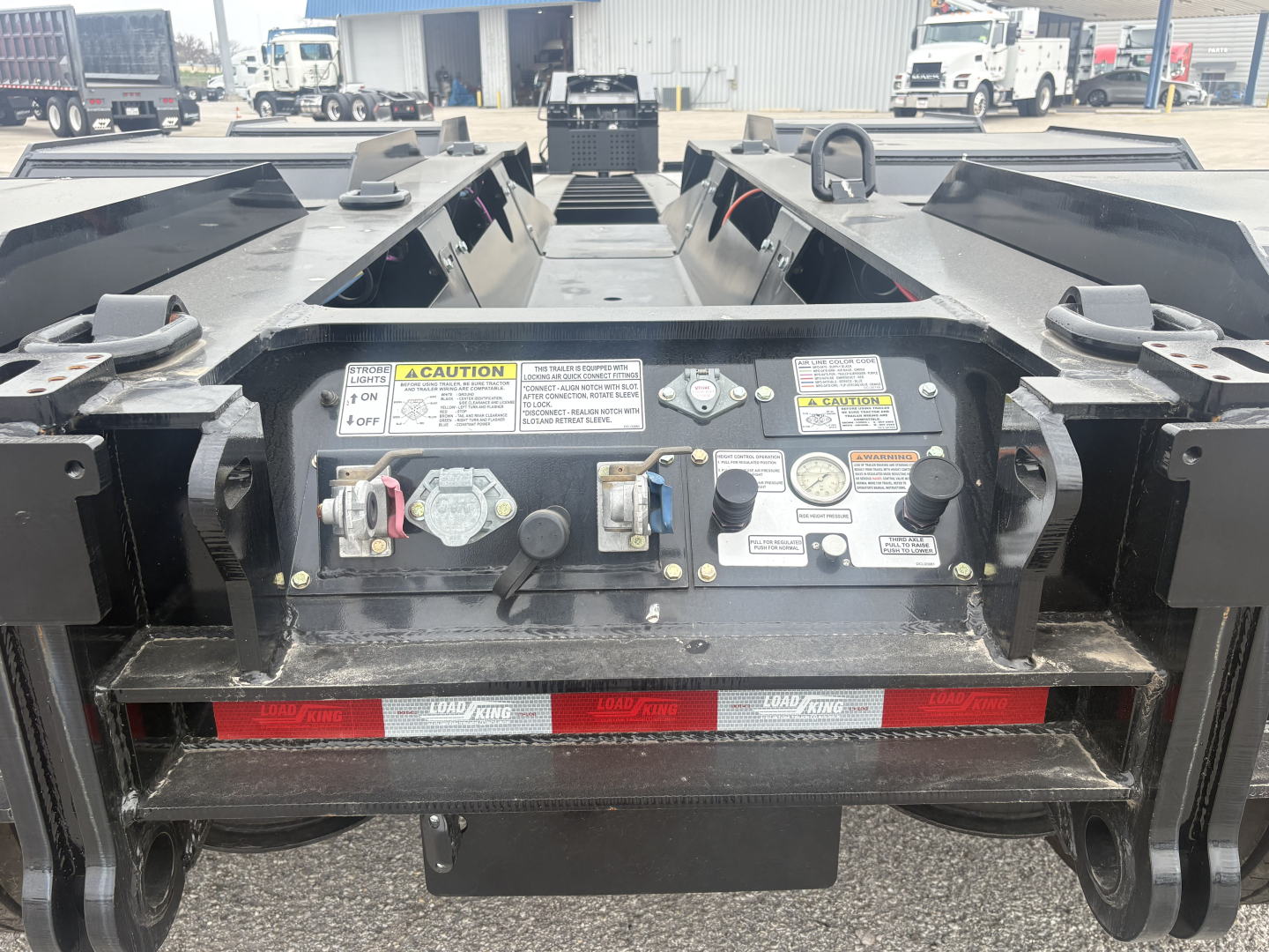 Load King trailer rear control panel and warning labels with hydraulic controls, safety decals, anti-slip paint, and coupling area in view.