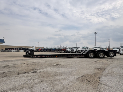 Load King lowboy trailer showing multiple axles and long low deck with ramps, side rails, and labeling visible on trailer surface.