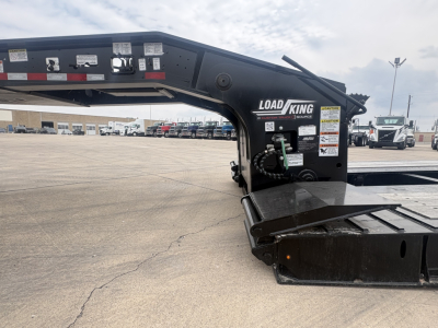 Load King lowboy trailer kingpin area with deck and hydraulic component mounts, black metal structure, white warning stickers, and extended beams.