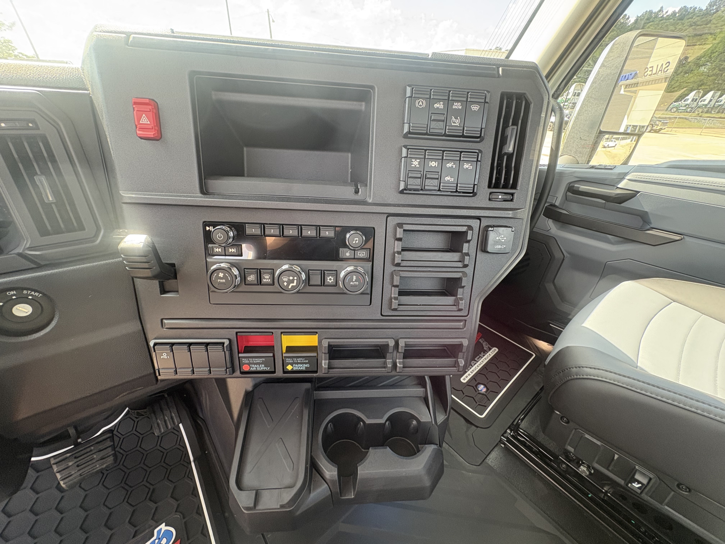 Dashboard and center console of a Mack AN64T truck cab showing controls, climate dials, USB blocks, cup holders, and storage compartments.