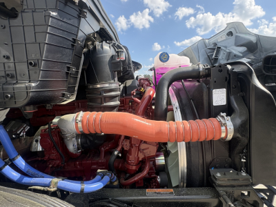 Truck engine bay close-up showing orange flexible coolant hose connected to radiator and surrounding blue hoses; visible radiator and engine components
