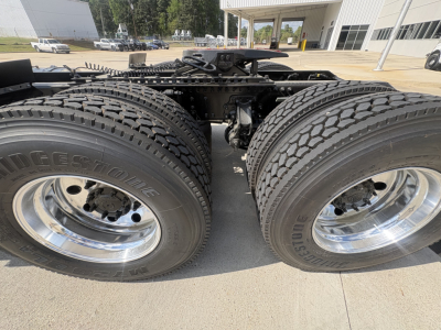 Dual rear tractor wheels with heavy-duty tires and chrome rims on a Mack AN64T cab chassis, showcasing the drive axles and suspension mounting area.