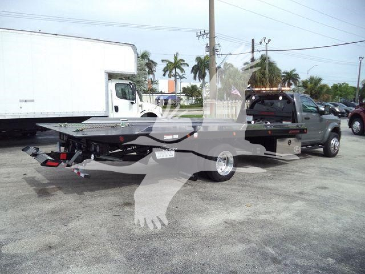 Ram 5500 rollback truck with flatbed, side view showing hitch and trailer connectors, rear lights, and branding not fully visible.