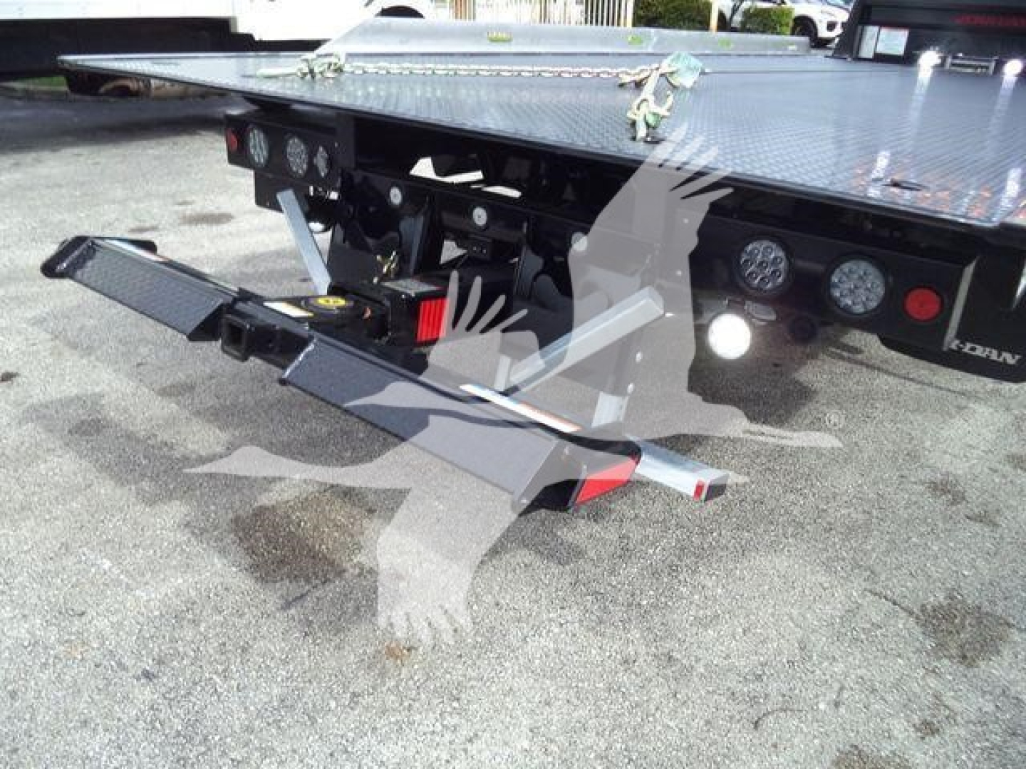 Ram 5500 rollback truck with tilted hydraulic wheel lift and flatbed, rear view showing loading ramps and bumper lights.