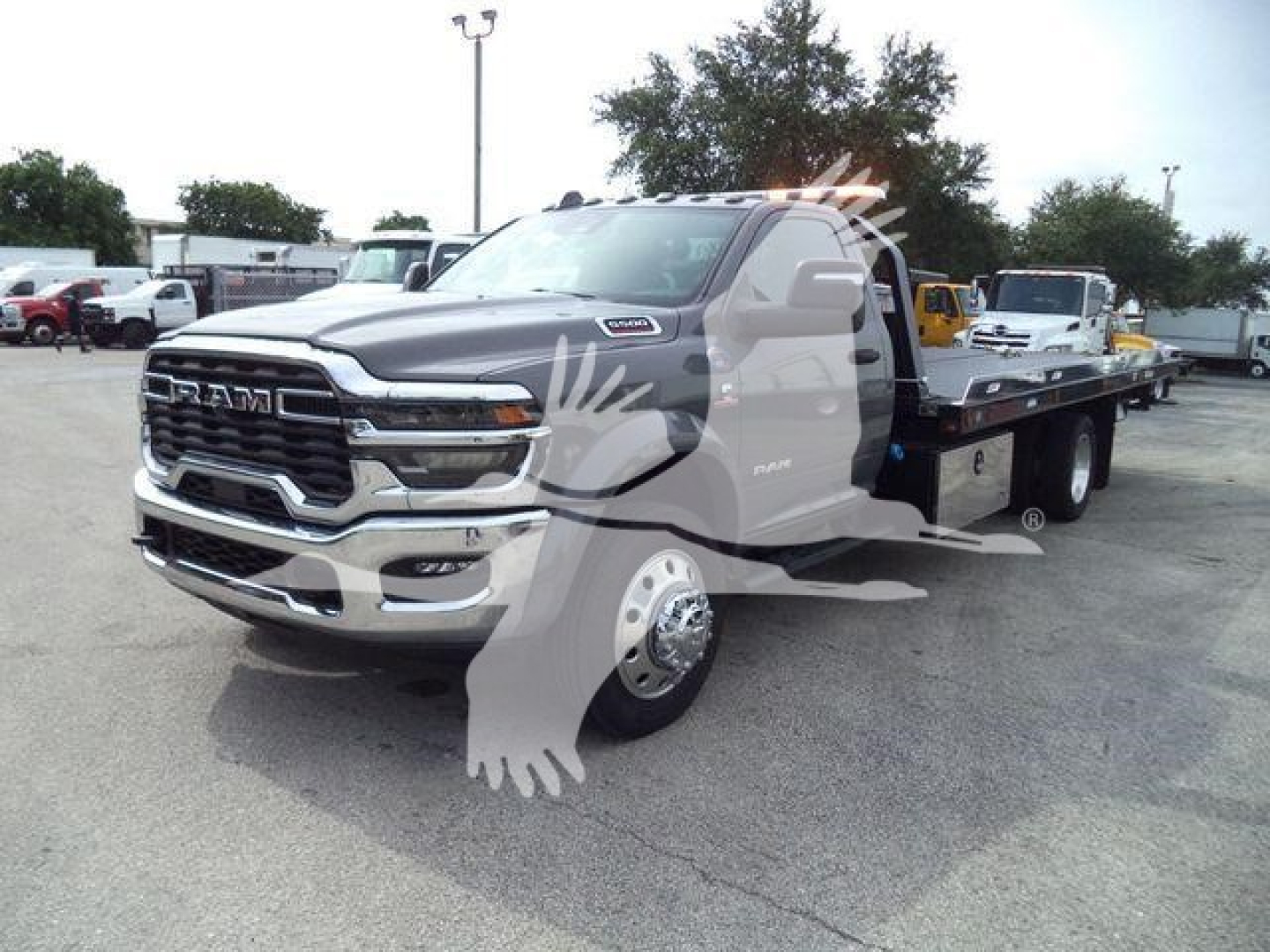 Ram 5500 rollback tow truck in metallic gray with extended flatbed, front grille RAM logo and dual rear wheels, dealership lot background.