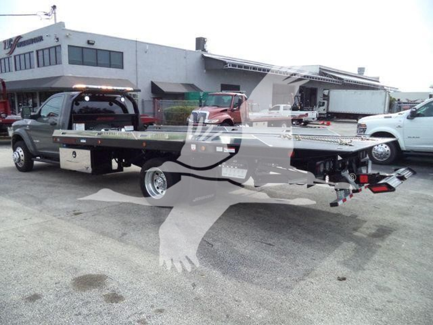 Ram 5500 rollback tow truck with flatbed viewed from rear/side showing long flatbed and towing equipment.