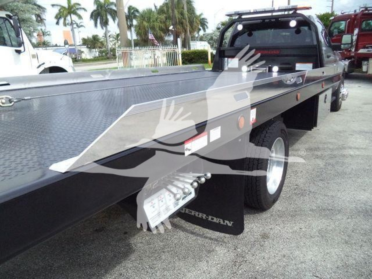 Ram 5500 rollback truck flatbed with metal diamond plate, tow hitch area, and wheel. Visible text includes 'RAM 5500' and control area near the cab, along with warning stickers and decals on the flatbed.