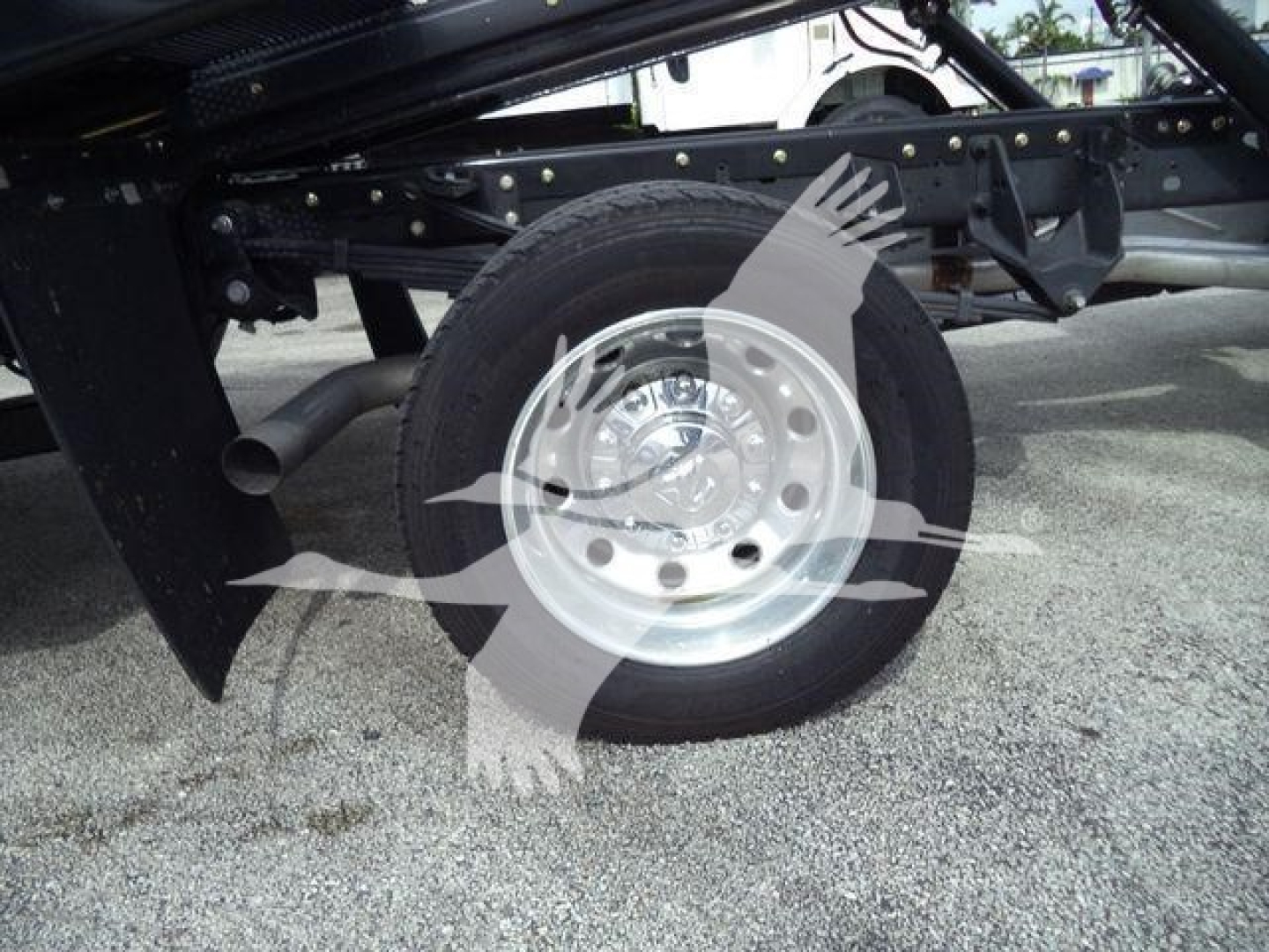 Front wheel and undercarriage of a Ram 5500 rollback truck showing a polished aluminum wheel and tire, frame rails, and hydraulic components.