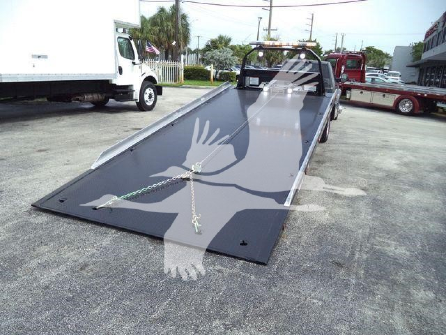 Truck bed with a lowered ramp tow setup on a Ram 5500 rollback, showing the long black deck and tie-downs.