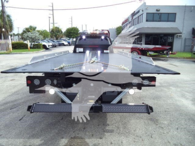 Flatbed tow truck in rear view showing hydraulic winch and steel bed with warning chains, Ram 5500 chassis hints in background.