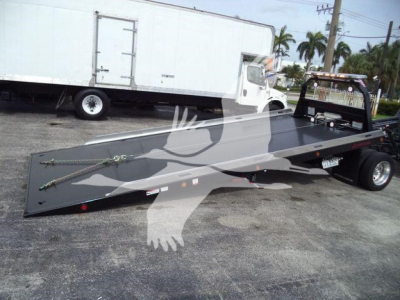 Flatbed rollback tow truck with long aluminum bed and wheel lift on a white cab, aftermarket equipment visible.