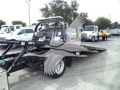 Flatbed rollback tow truck chassis with Ram 5500 Big Horn text not visible; background shows other trucks in a lot.