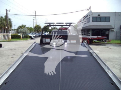 Ram 5500 rollback truck bed with metal diamond-plate surface and hitch area, rear view showing cab and equipment in background.
