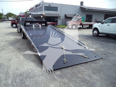 Ram 5500 rollback flatbed truck in a dealership yard with a long steel ramp and chain hooks visible.
