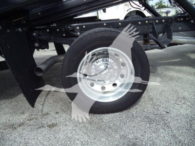 Front wheel and undercarriage of a Ram 5500 rollback truck showing a polished aluminum wheel and tire, frame rails, and hydraulic components.
