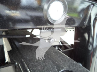 Trucking equipment component showing a round light and steel mounting with a winch or support arm; visible surface is black with some GRAY residue.