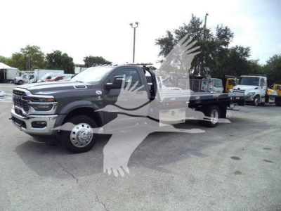 Ram 5500 rollback truck in a dealership lot with a long flatbed; front grille, dual rear wheels visible.