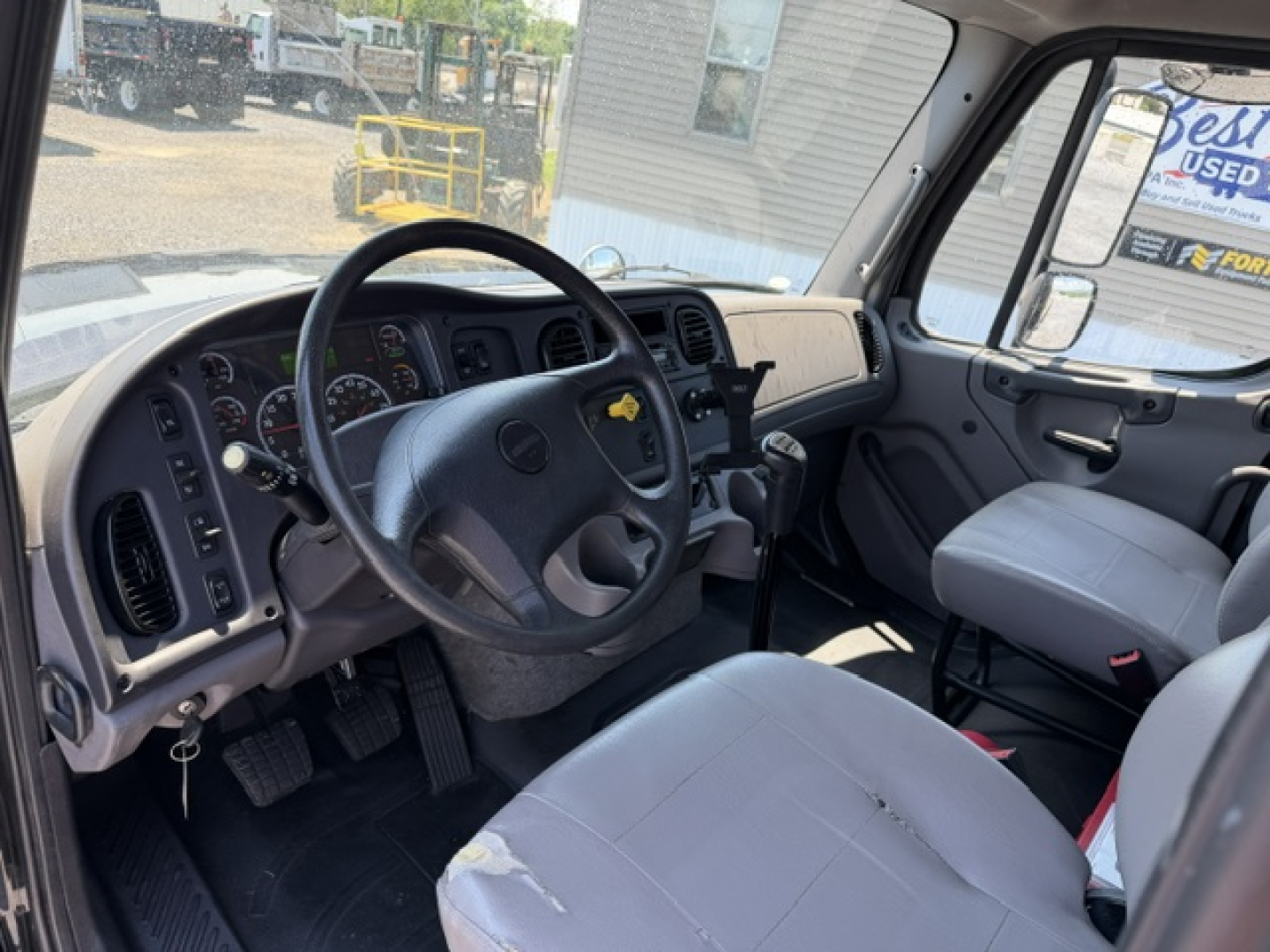 Truck cab interior of a 2016 Freightliner M2-112 showing steering wheel, dashboard, and gray fabric seats.