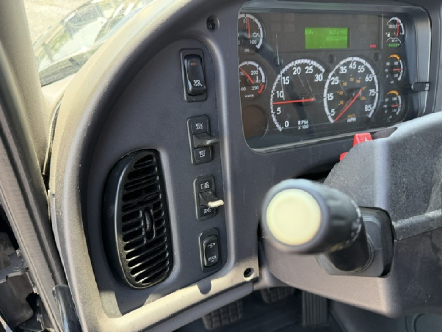 Cab interior of a Freightliner M2-112 showing steering column, instrument cluster with gauges, and control switches on the left dash.
